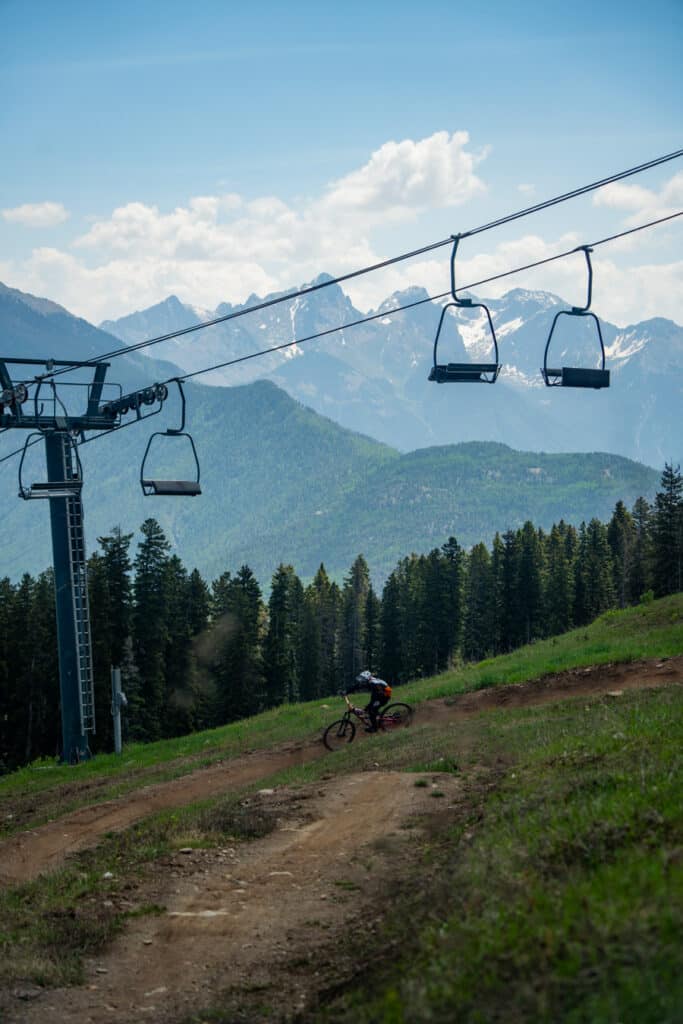 A mountain bikers rides a berm under a chairlift with mountains in the background at Purgatory Resort