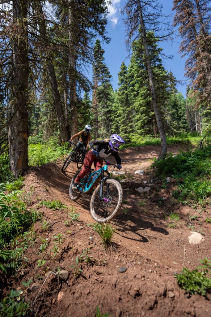 mountain bikers ride a berm on a trail at Purgatory resort